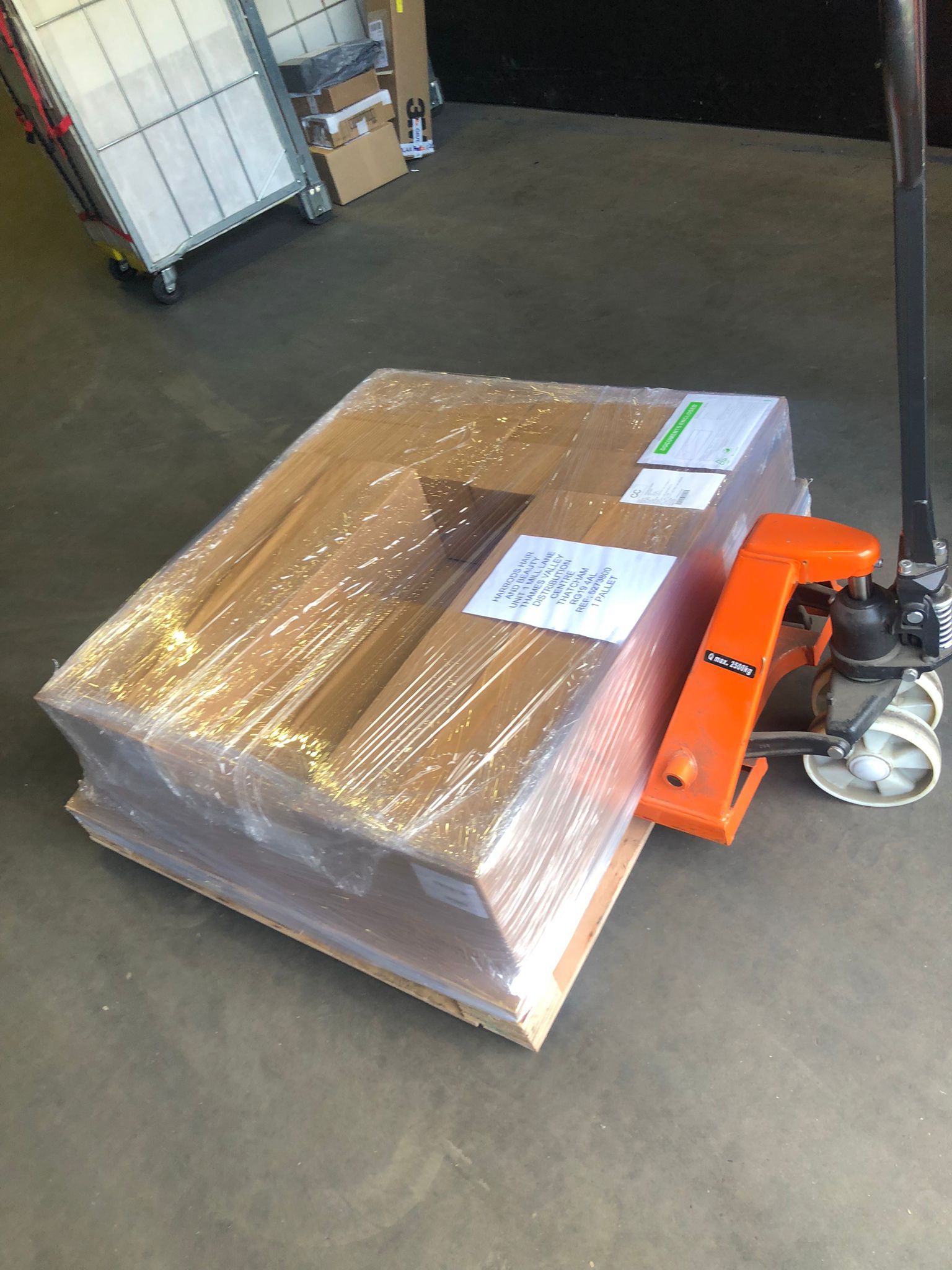 Wrapped pallet on a warehouse floor beside an orange pallet jack