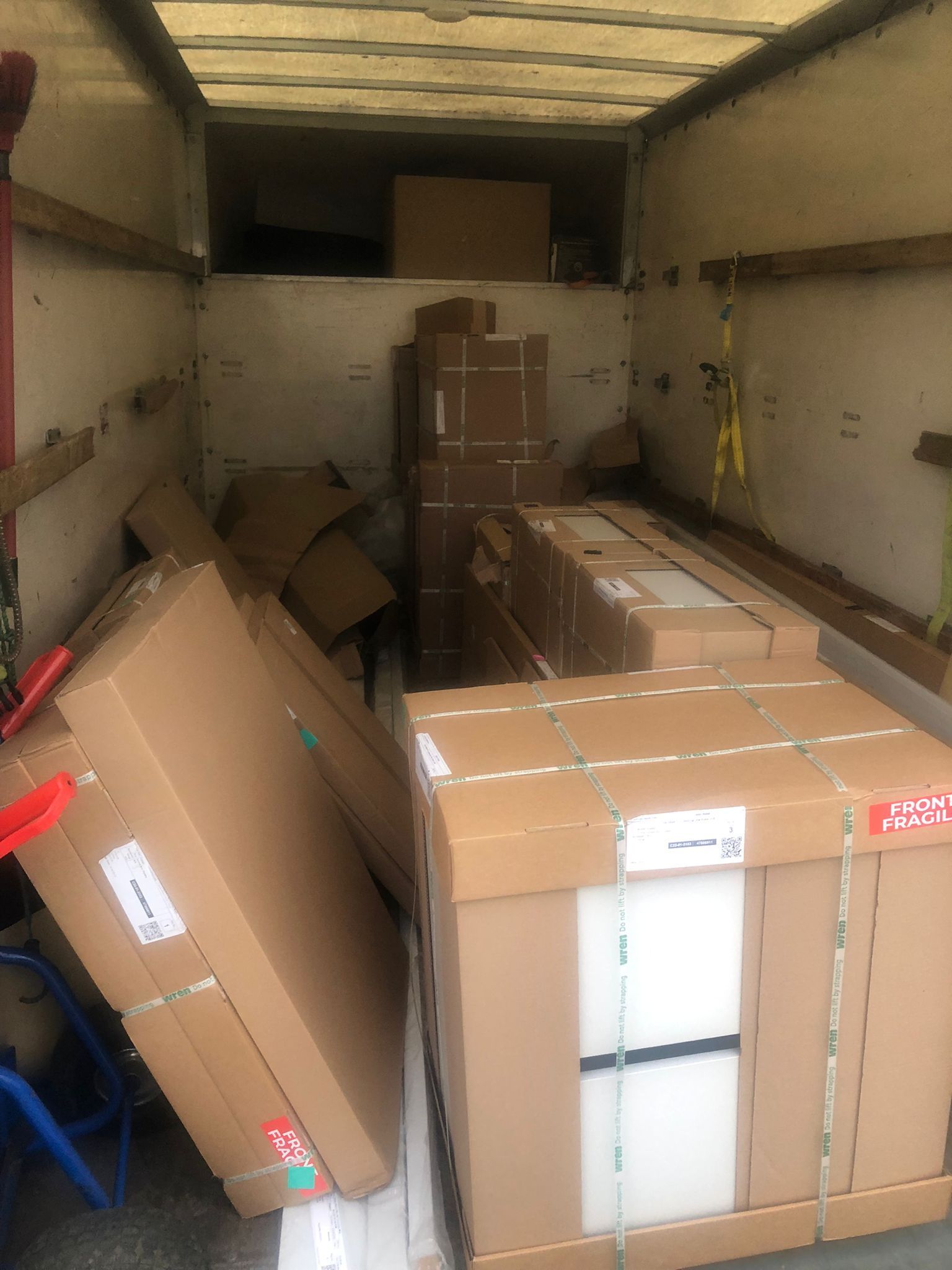 Cargo truck interior filled with cardboard boxes and wrapped parcels, some leaning along the walls.