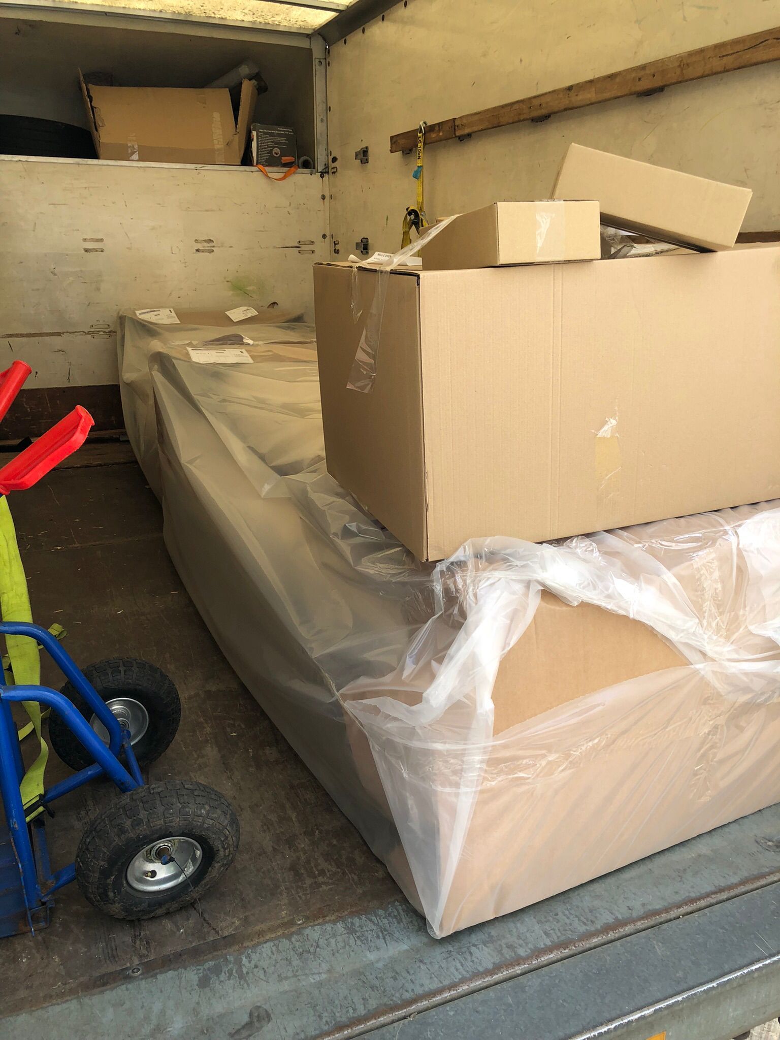 Cardboard boxes and wrapped furniture packed inside a moving truck, with a blue dolly at left.