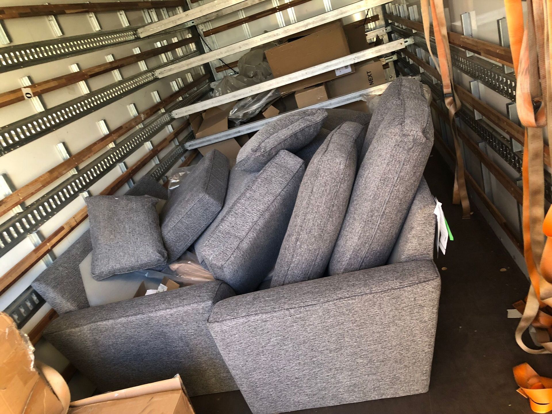 Gray upholstered sectional sofa piled with matching cushions inside a storage truck or trailer