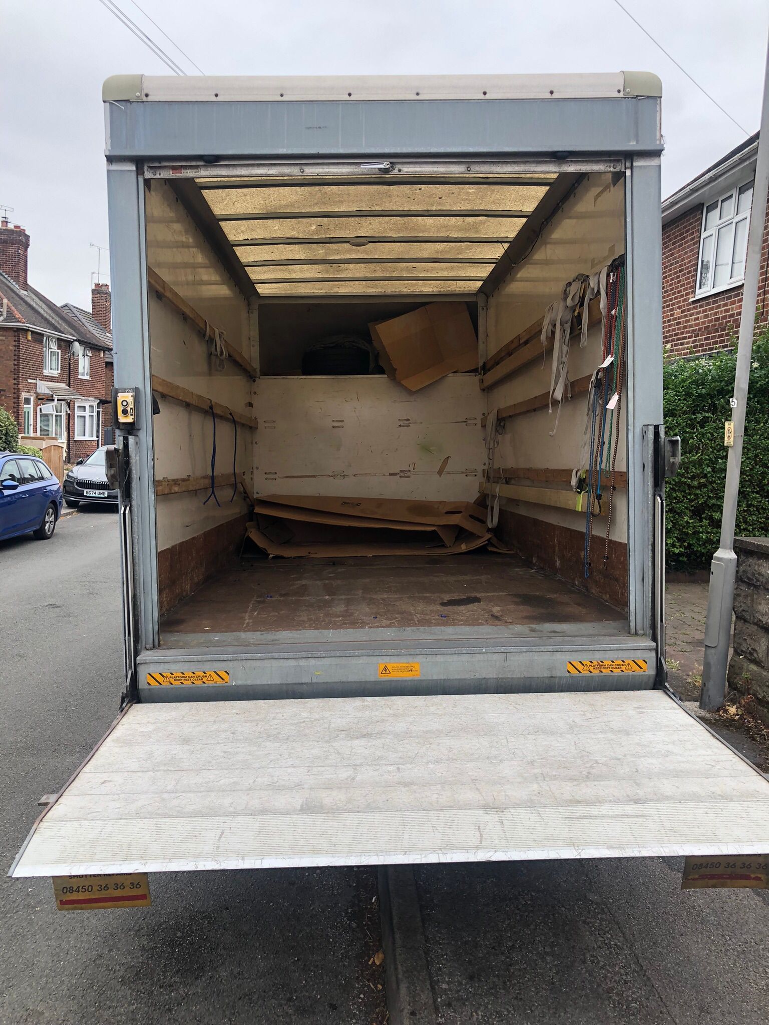 Open delivery truck with lowered ramp, mostly empty inside on a residential street.