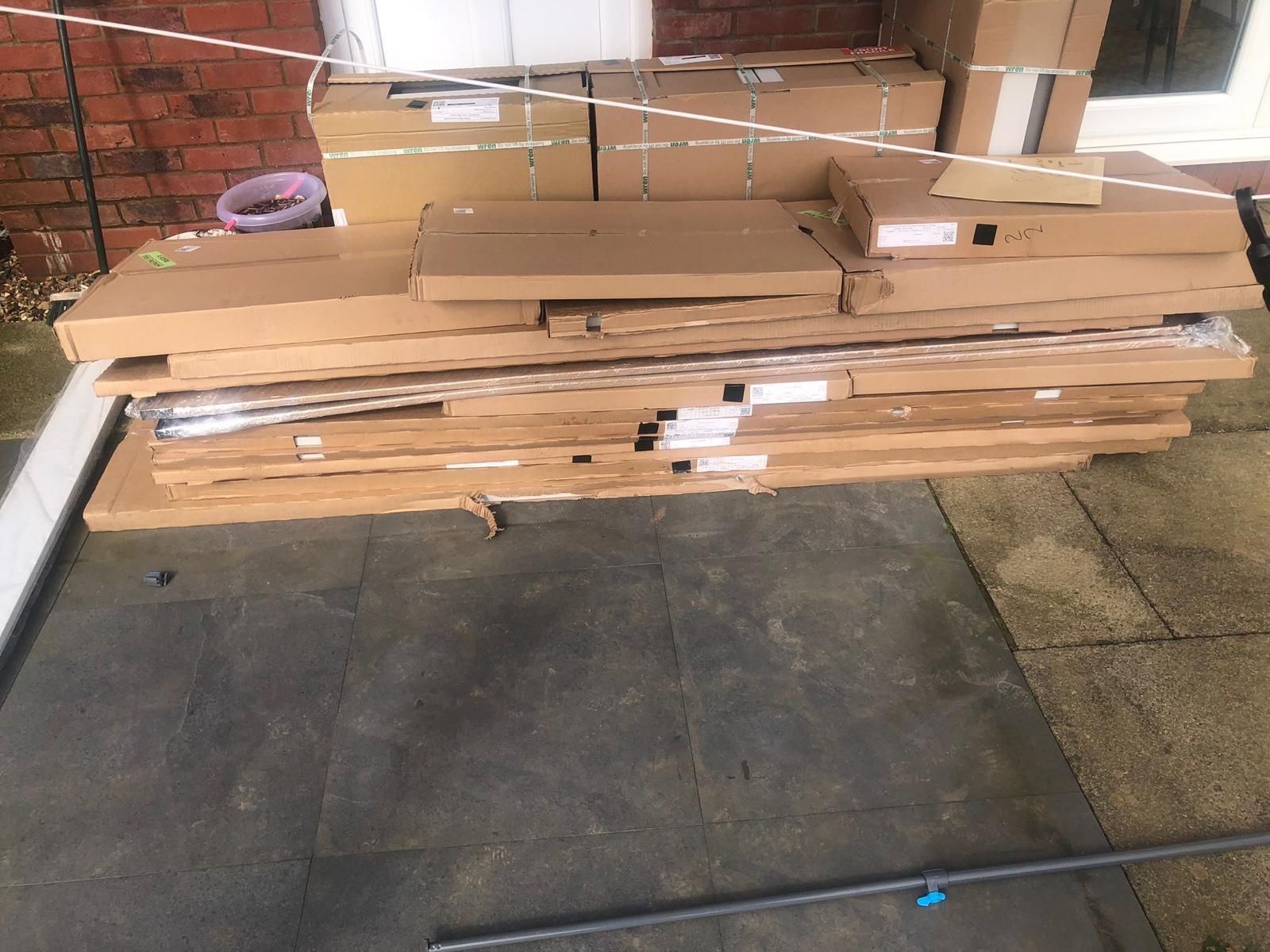 Stacked cardboard sheets and wooden boards leaning against a brick wall on a concrete floor.