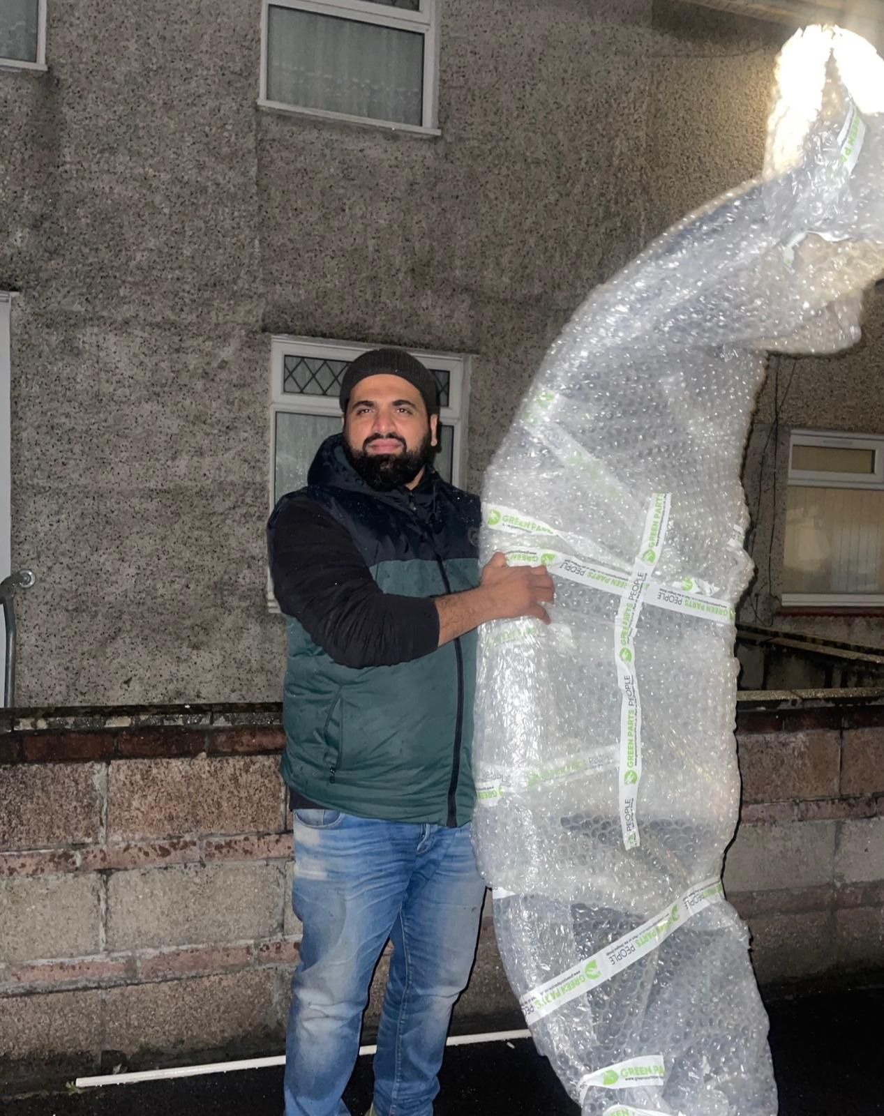 Man holding a large bubble-wrapped item beside a building at night