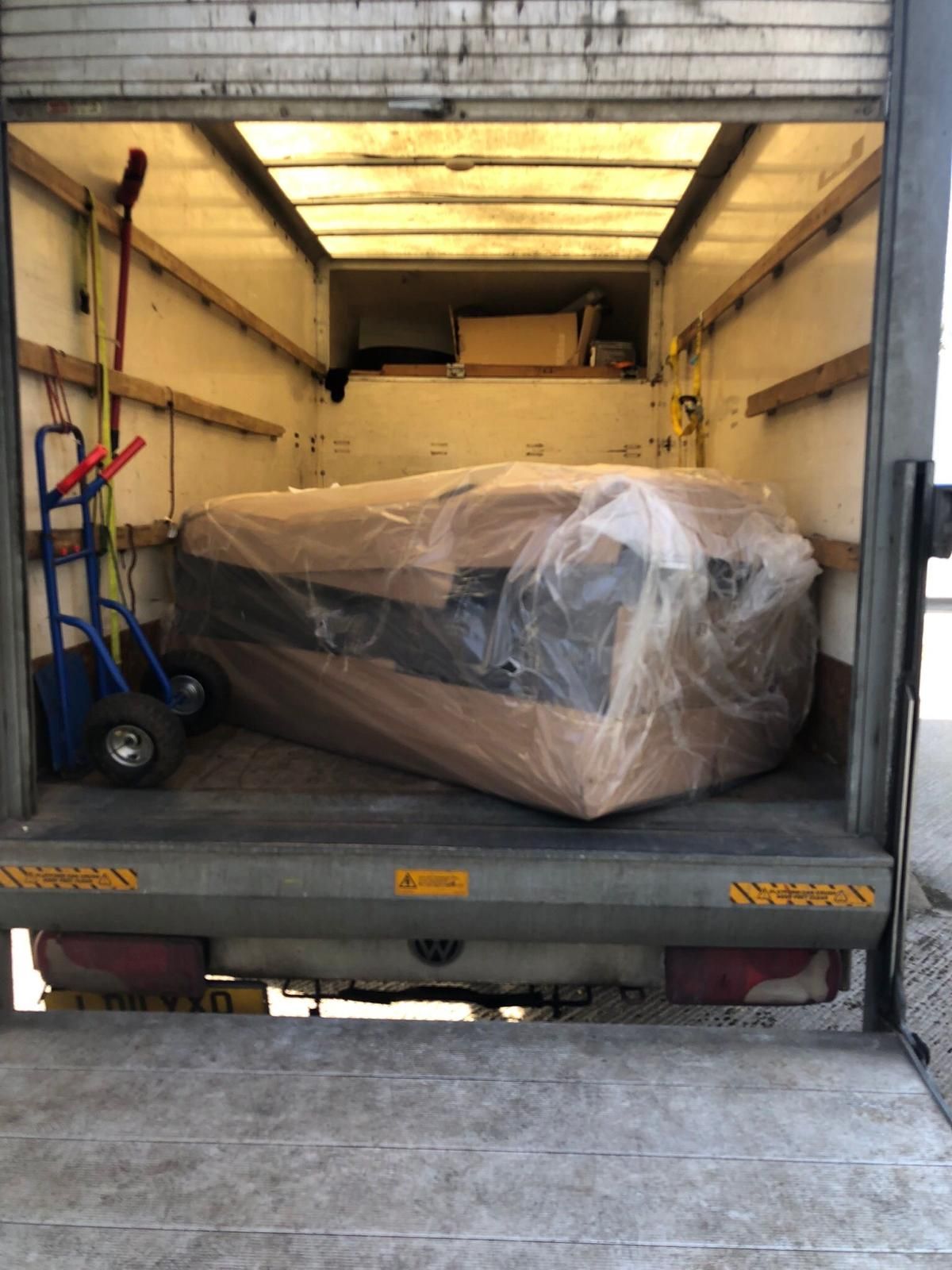 Moving truck interior with a wrapped sofa and hand truck, viewed from the open back.
