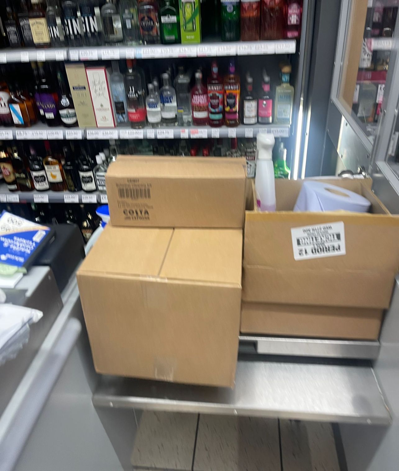Cardboard boxes on a store counter with shelves of drinks in the background.