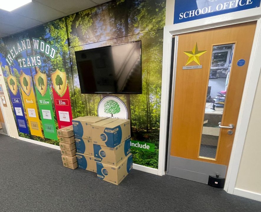 School office hallway with TV, woodland mural, and stacked cardboard donation boxes by the door