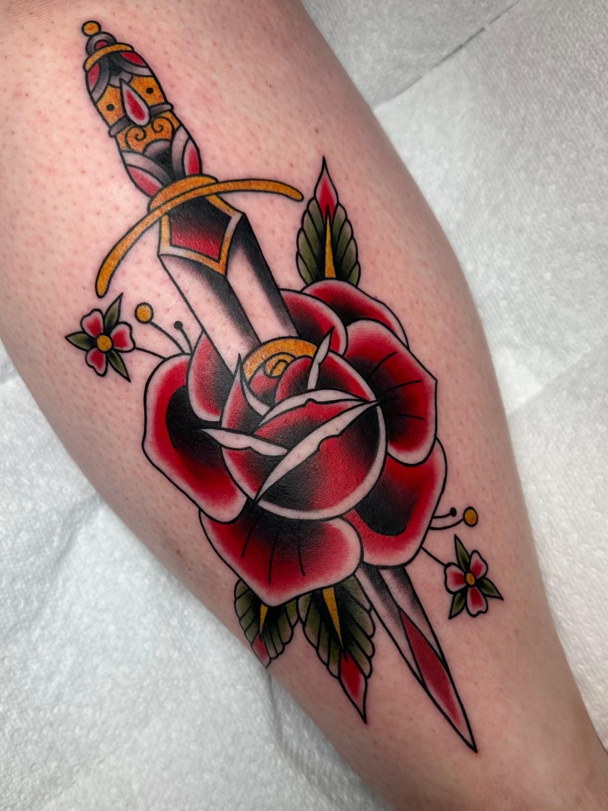 A tattoo of a dagger and a rose on a leg