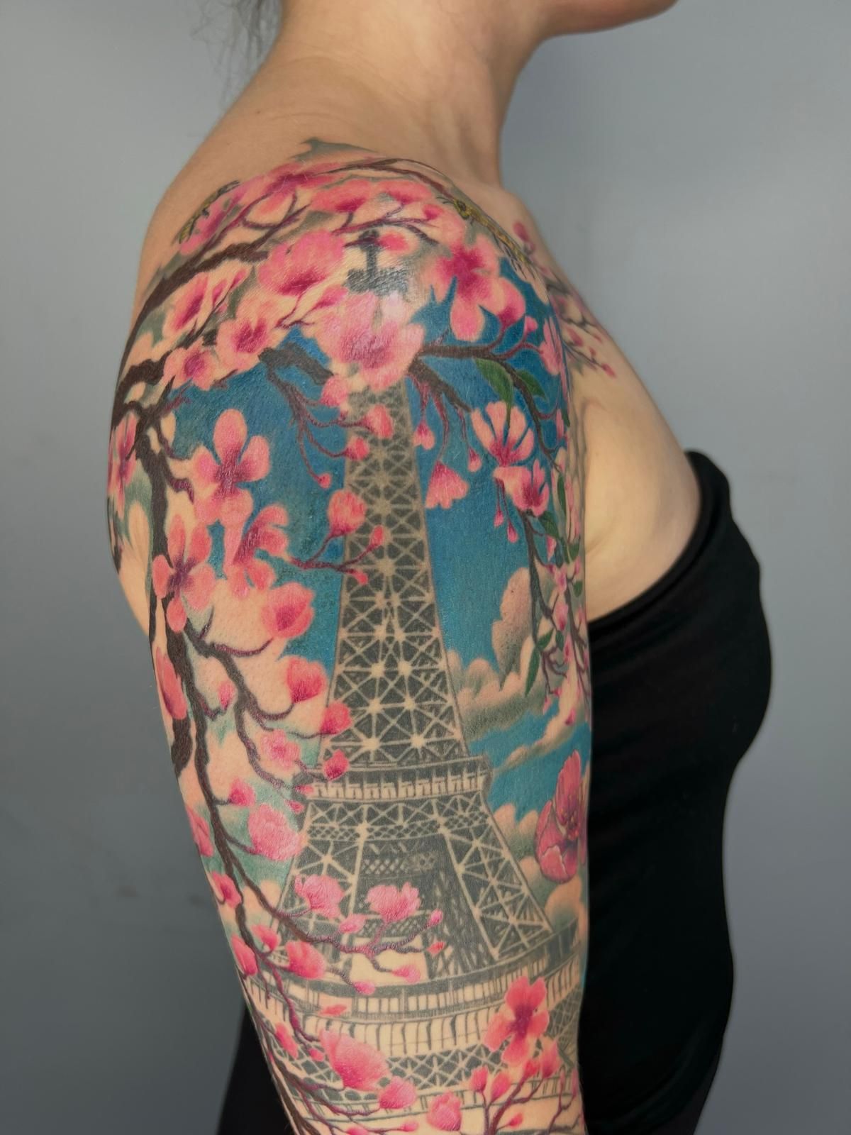 A woman has a tattoo of the eiffel tower and cherry blossoms on her arm