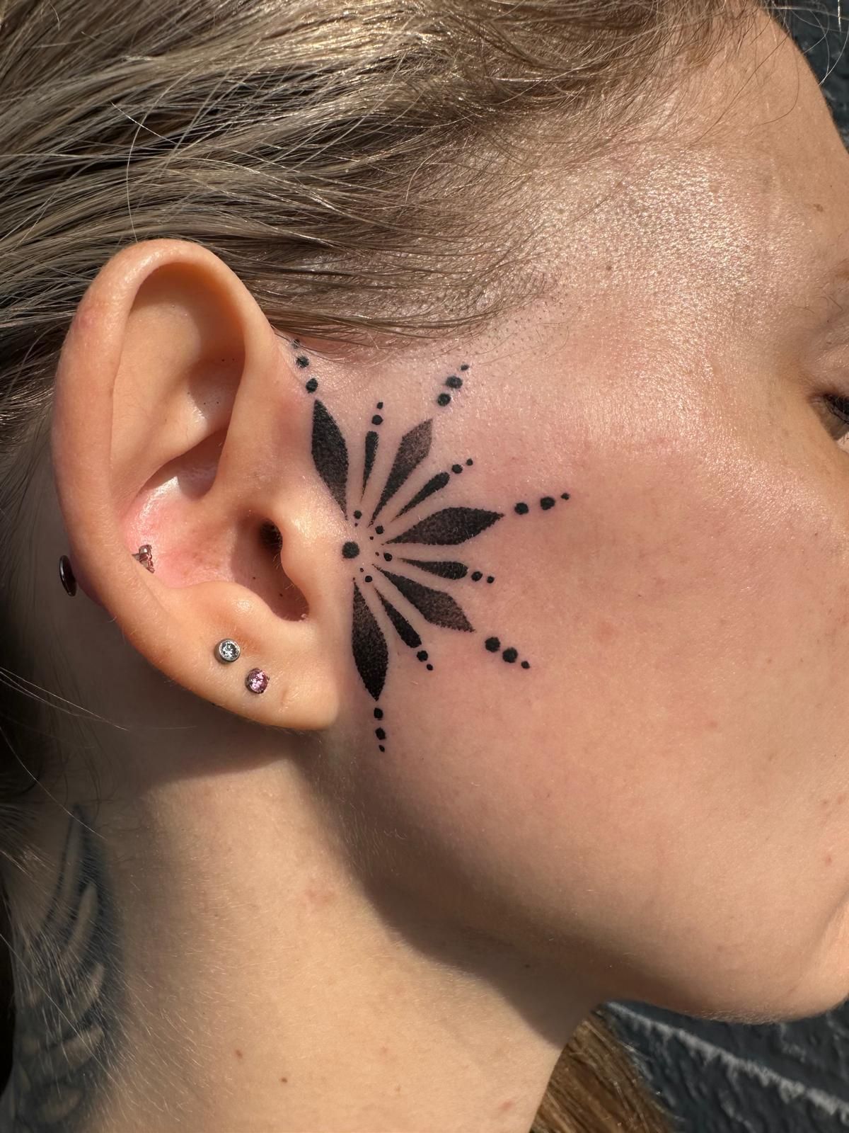 A woman has a tattoo on her face behind her ear.