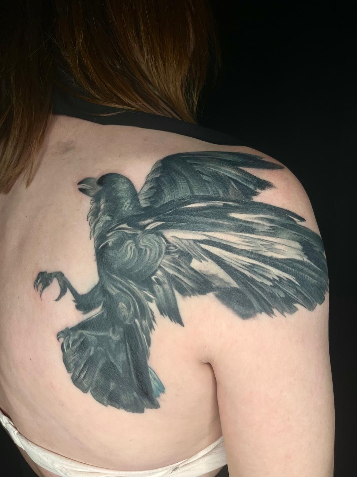 A woman has a tattoo of a crow on her back