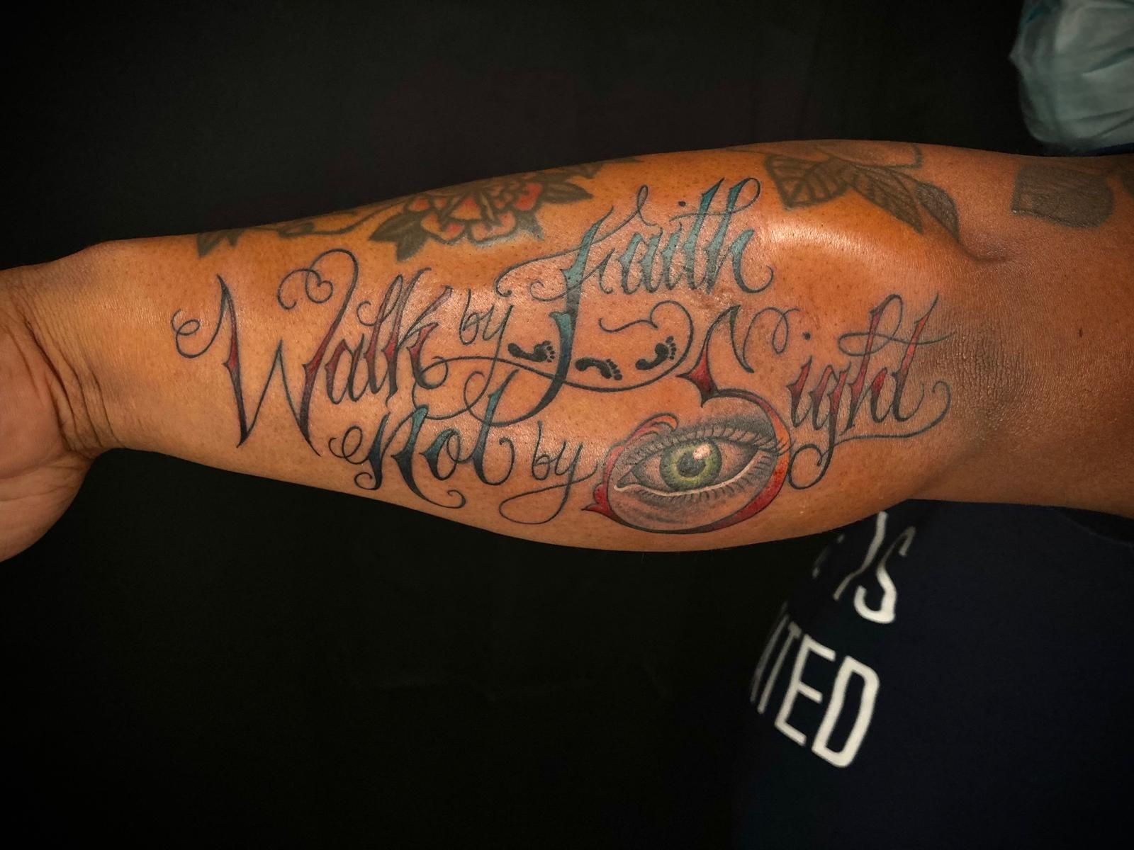 A man has a tattoo on his arm that says walk by faith not by sight