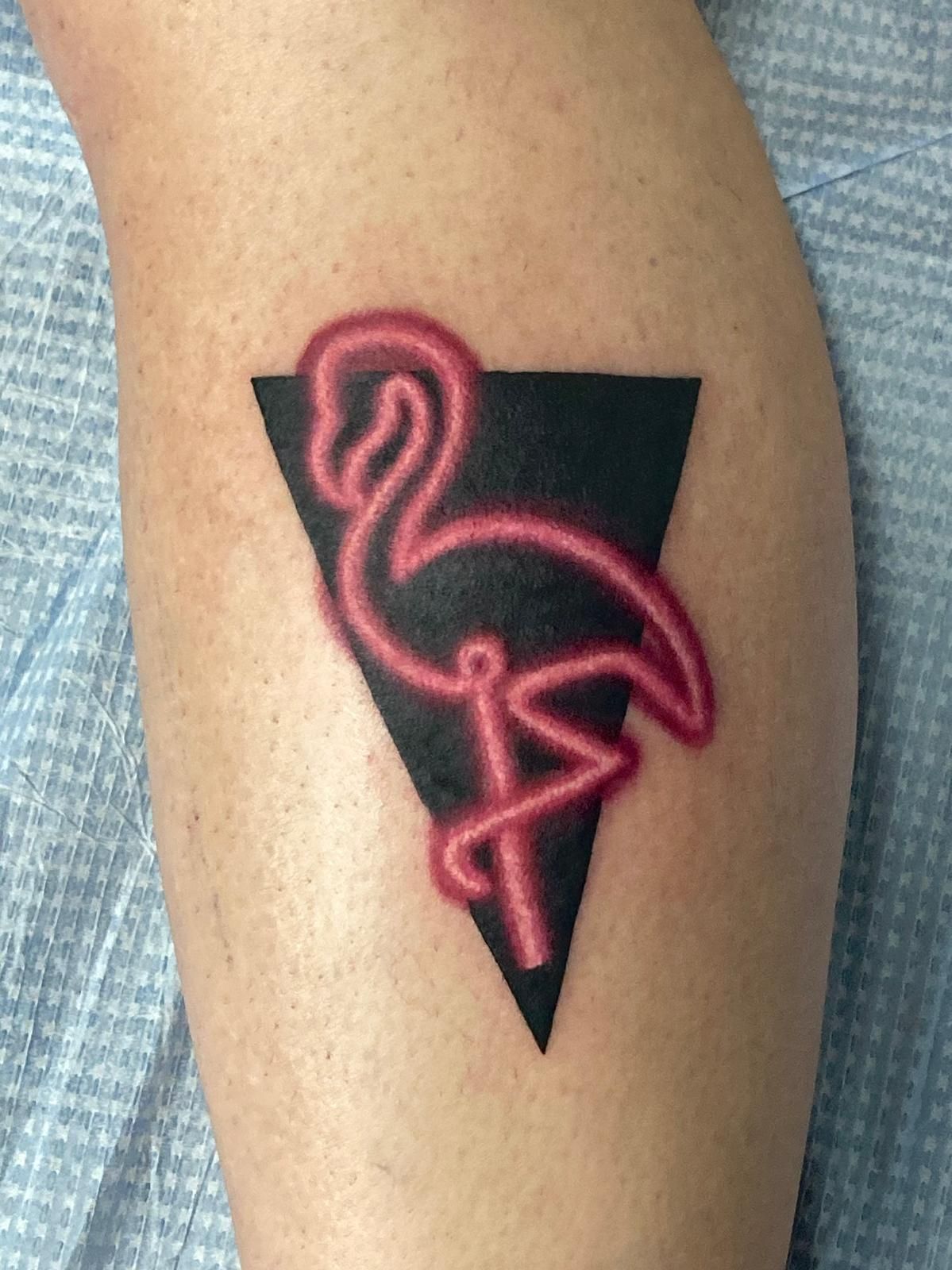 A person has a neon flamingo tattoo on their leg