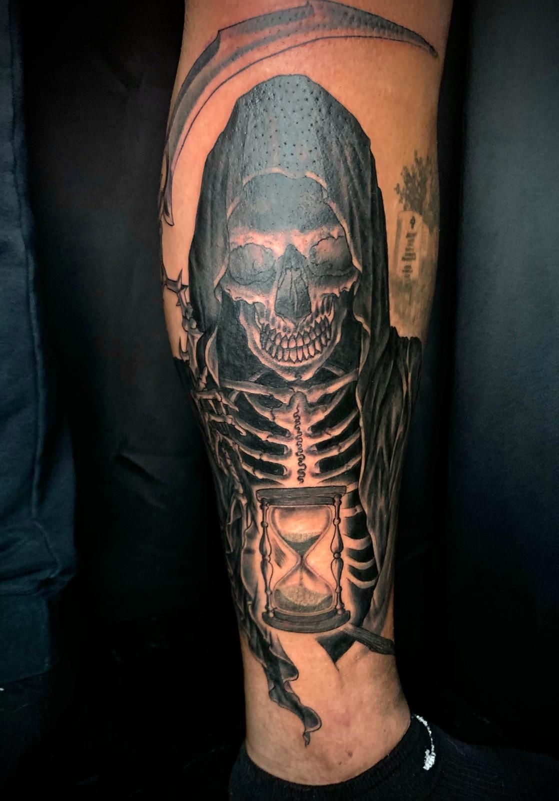 A person has a grim reaper tattoo on their leg.