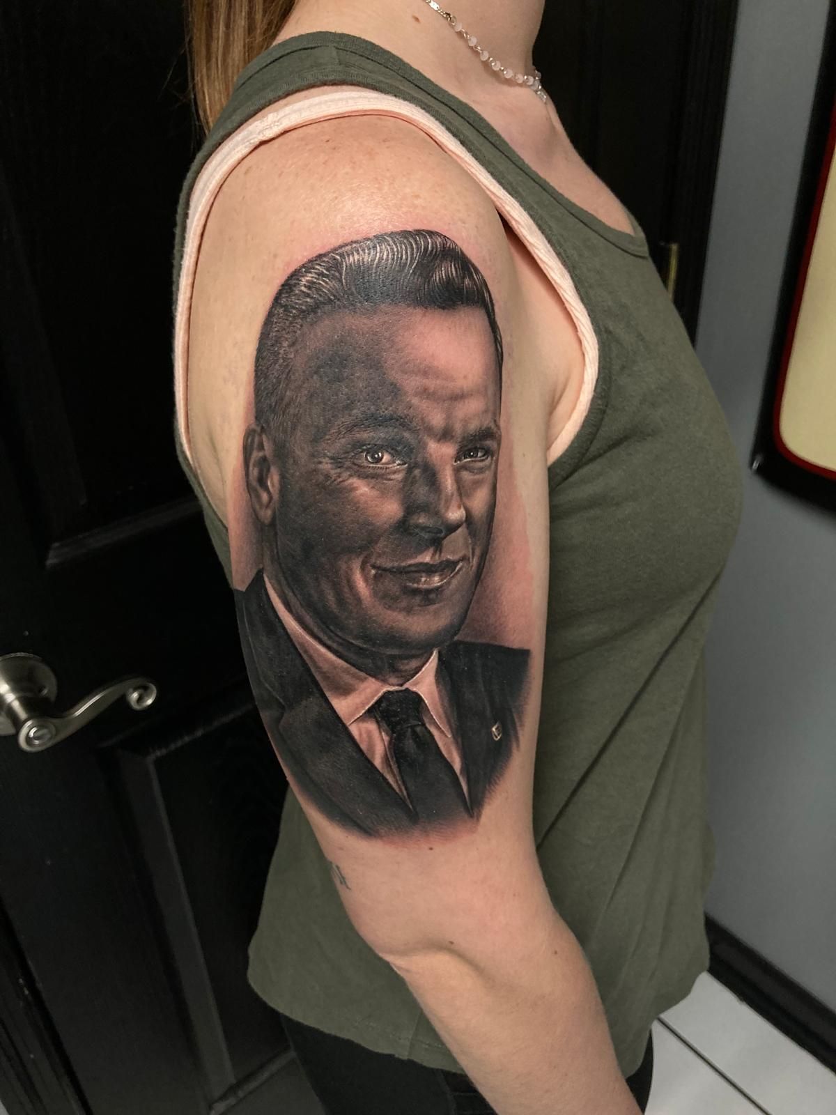 A woman has a tattoo of a man in a suit and tie on her arm