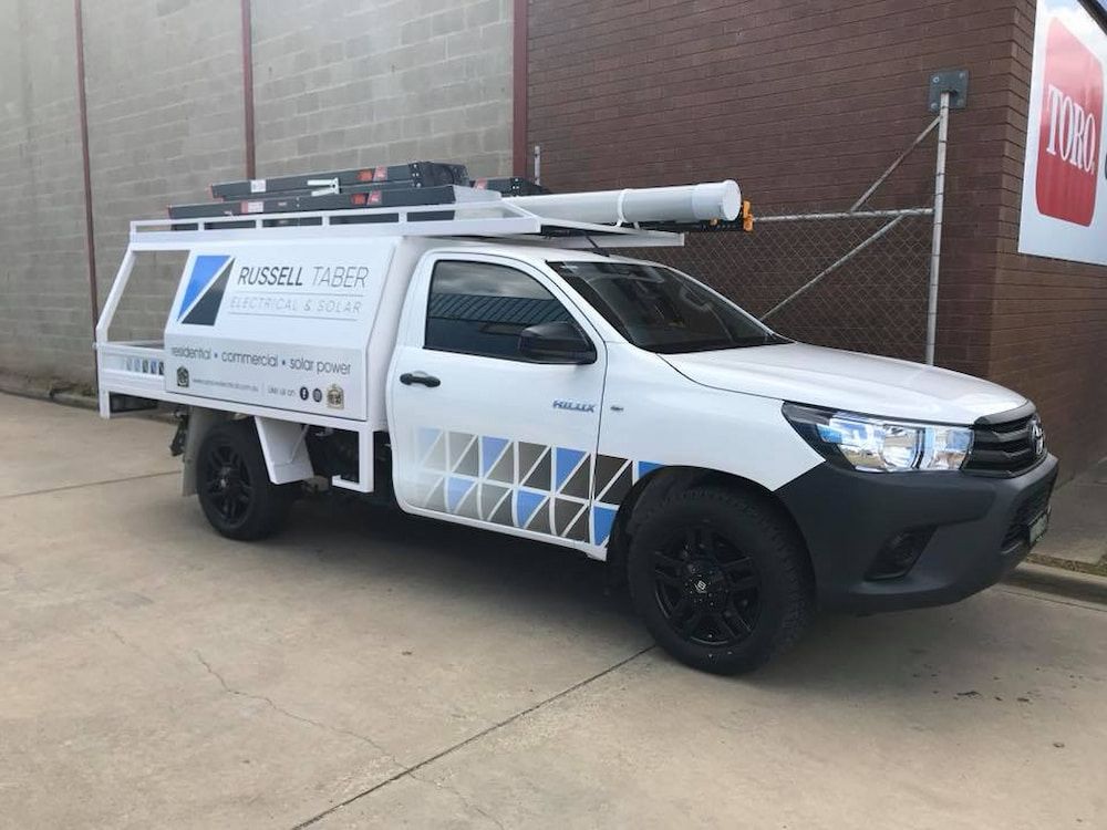 A White Truck is Parked in Front of a Brick Building — Russell Taber Electrical & Solar in Lake Albert, NSW