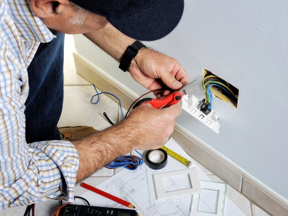 A Man is Working on an Electrical Outlet With a Pair of Pliers — Russell Taber Electrical & Solar in Lake Albert, NSW