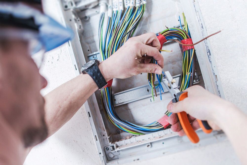 A Man is Working on an Electrical Box With a Pair of Pliers — Russell Taber Electrical & Solar in Lake Albert, NSW