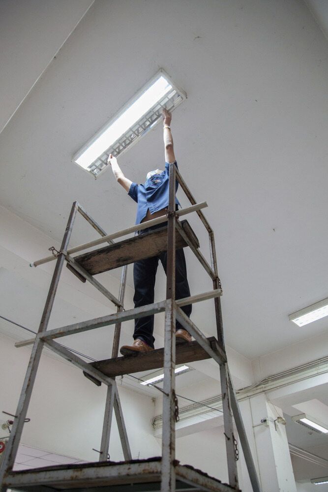 A Man is Standing on a Scaffolding Fixing a Light Fixture — Russell Taber Electrical & Solar in Lake Albert, NSW