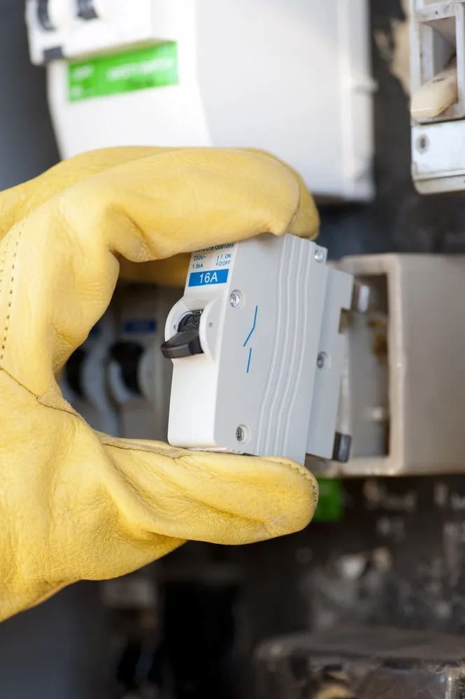 A Person Wearing Yellow Gloves is Holding a Circuit Breaker — Russell Taber Electrical & Solar in Lake Albert, NSW