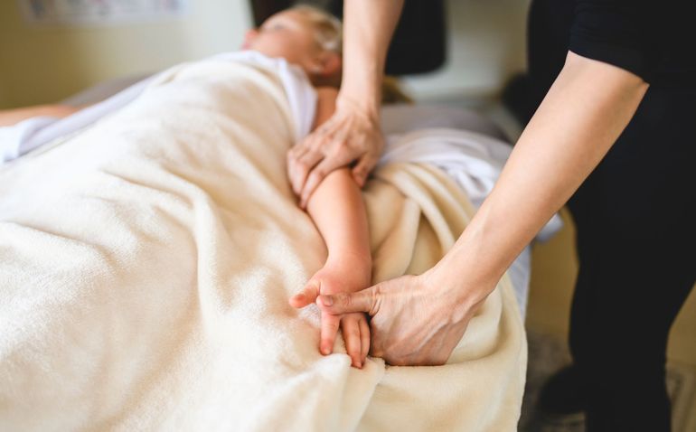 Hands massaging a person’s back under a beige blanket in a softly lit room