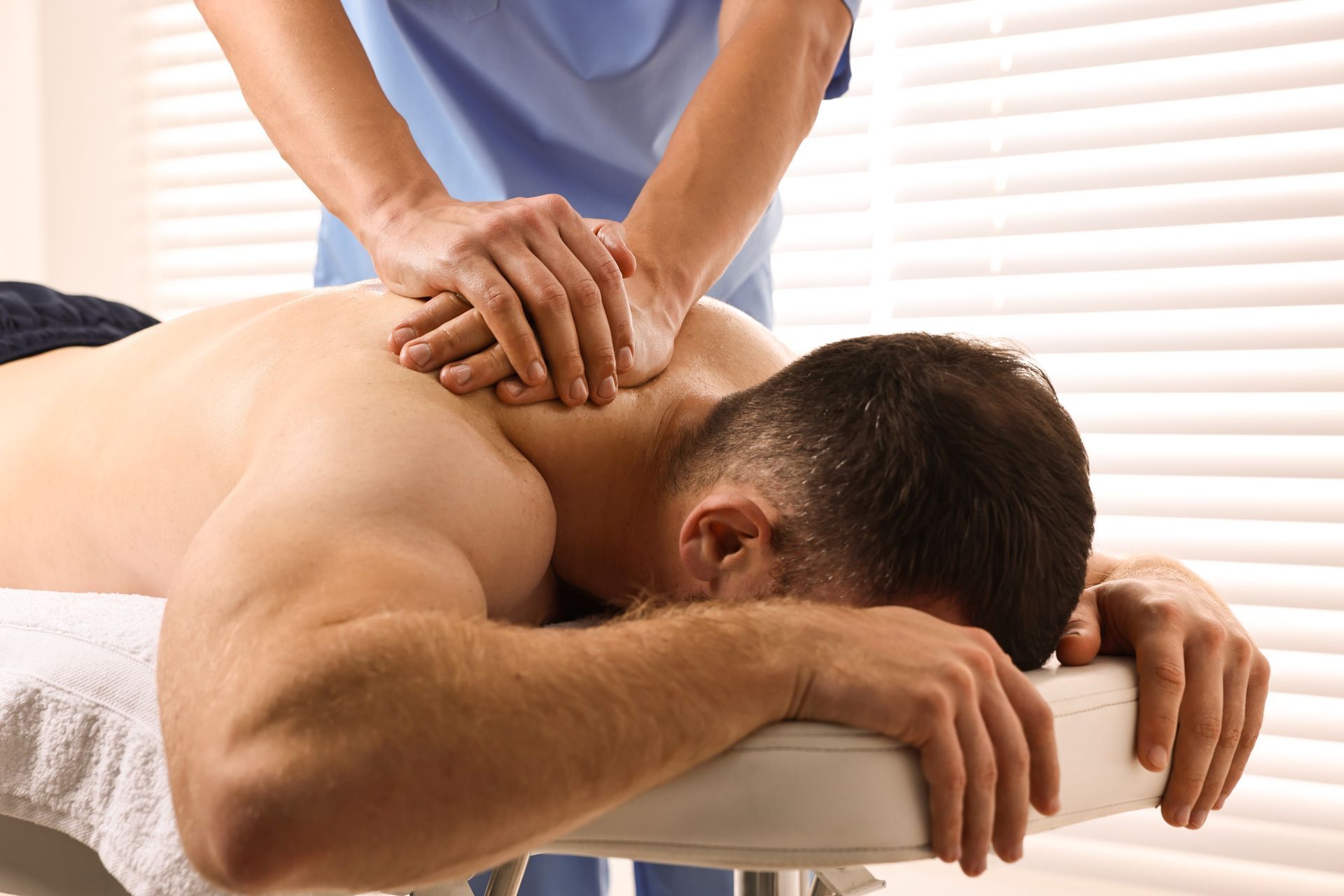 Massage therapist pressing a client's back on a massage table in a bright room