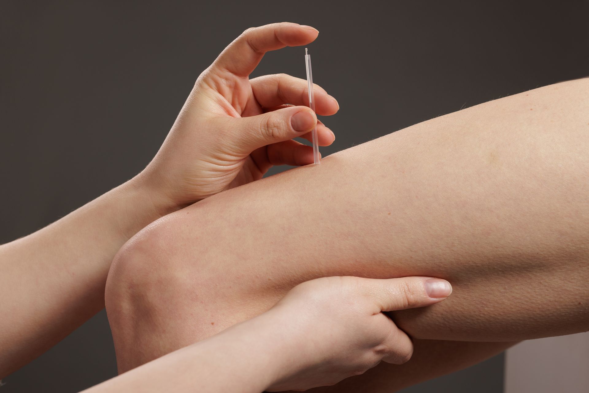 Hand holding a syringe near a bent leg, preparing an injection on skin.