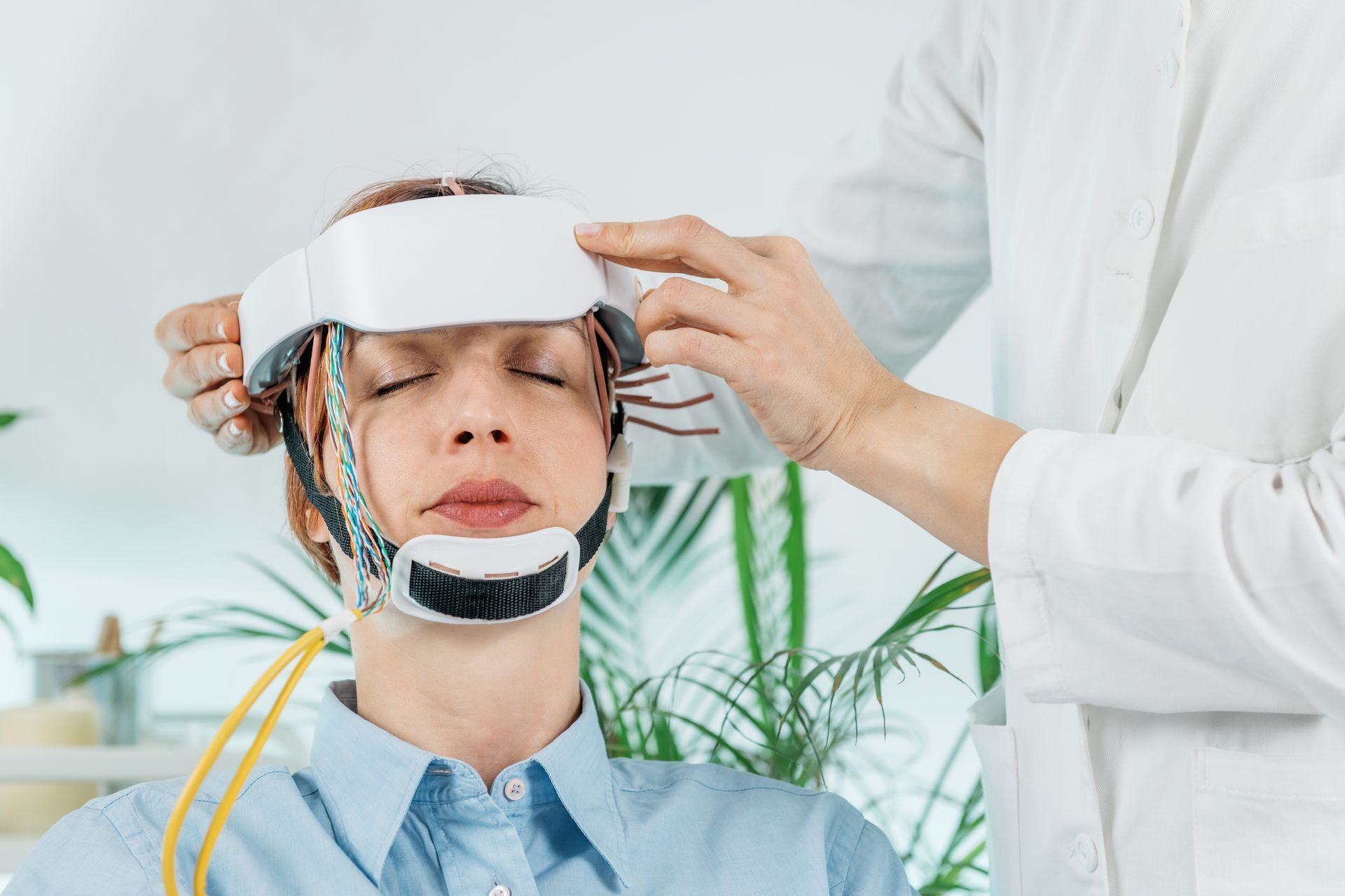 Person in medical headgear during a therapy or diagnostic treatment, with a clinician adjusting the device.