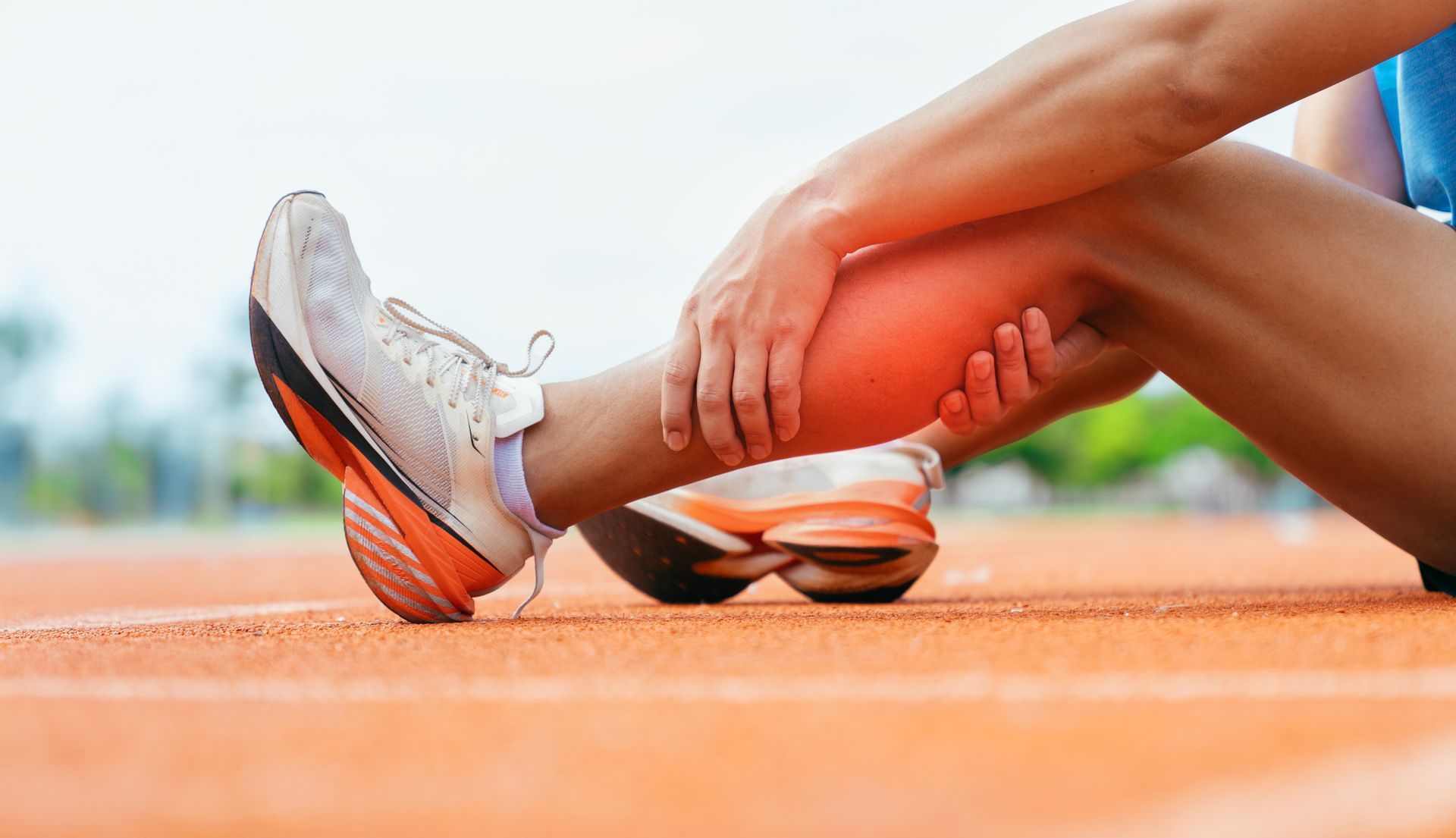 Runner stretching leg on orange track, wearing white sneakers.