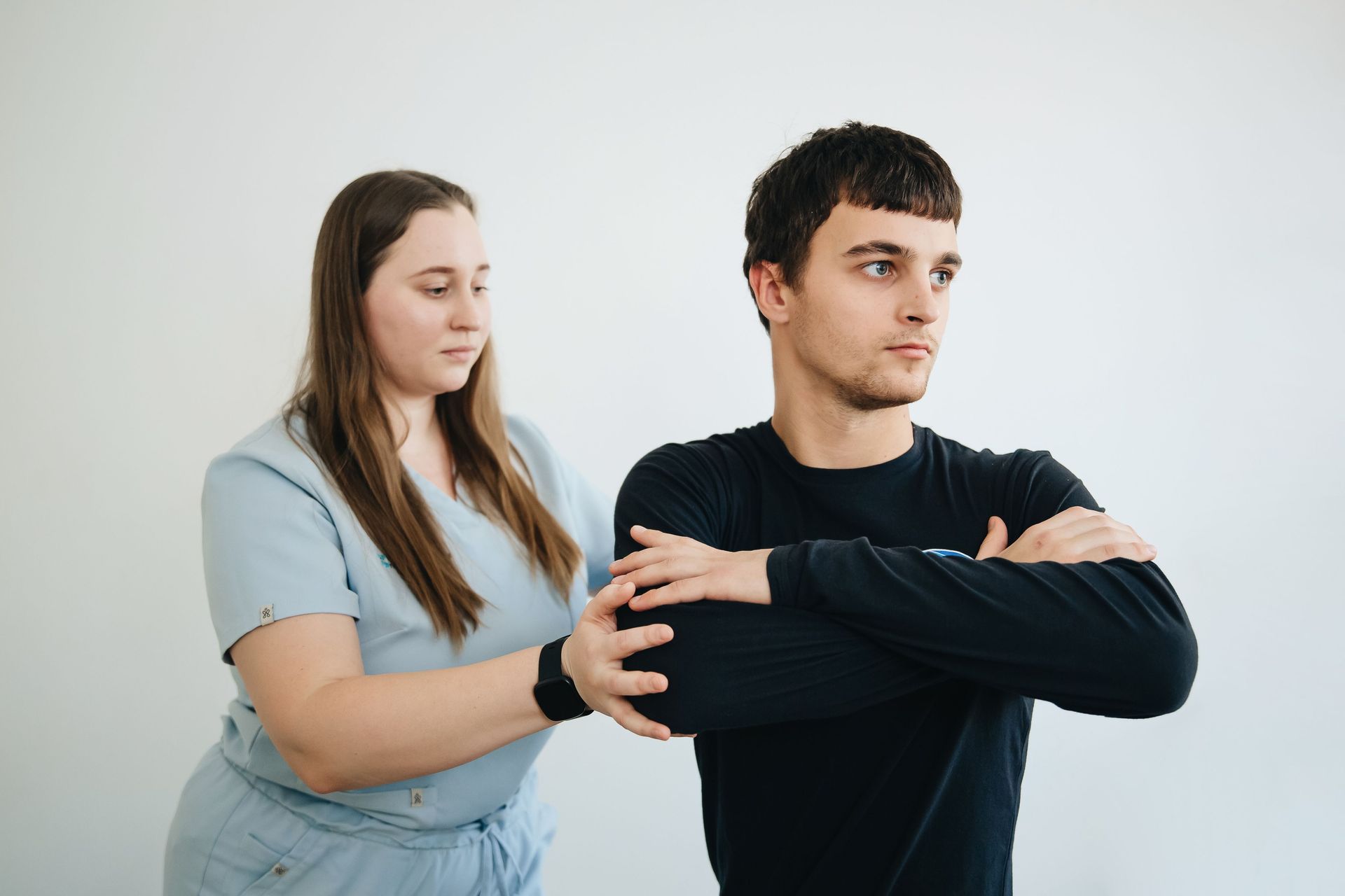 Two people in a light gray room, one standing behind the other with hands on shoulders as if guiding posture.