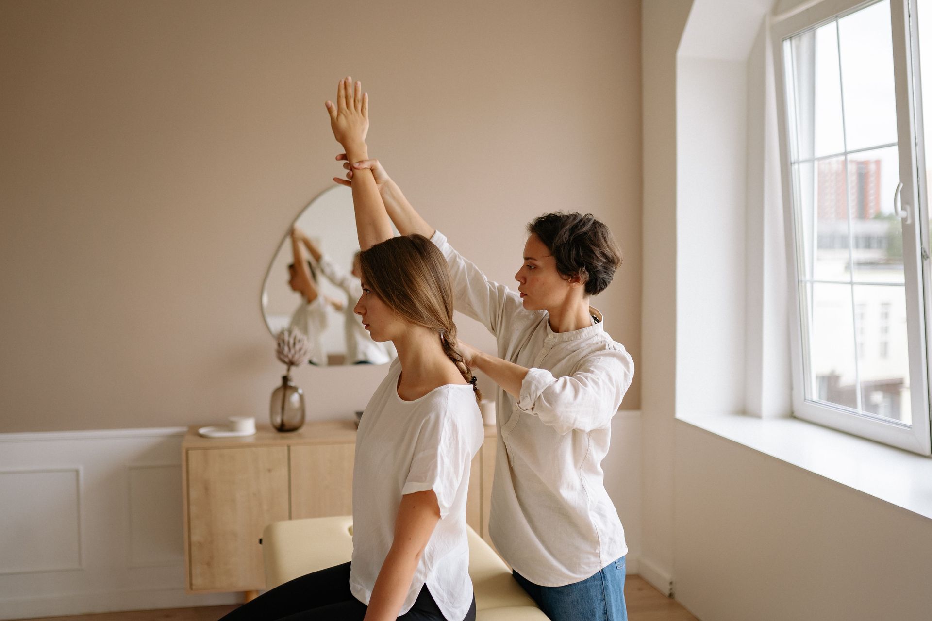 Two people stretching in a bright room near a window and mirror