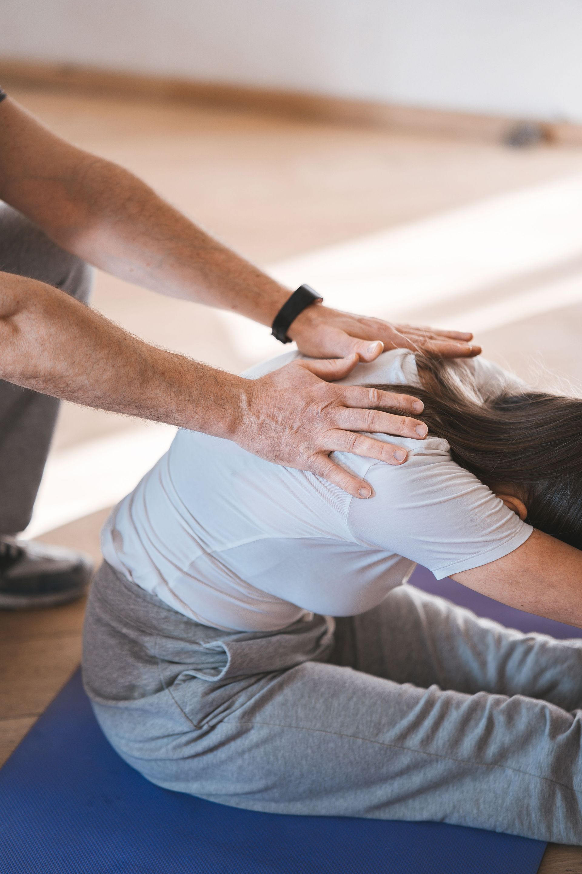 Physical therapist stretching a seated patient’s back on a blue mat in a studio