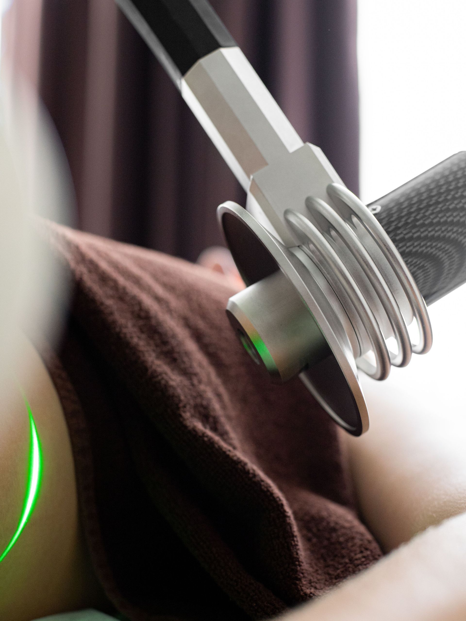 Close-up of a handheld massage device with metal prongs pressed against brown fabric on a bed