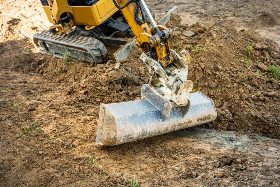 A yellow mini excavator with a metal bucket rests on a mound of loose brown dirt.