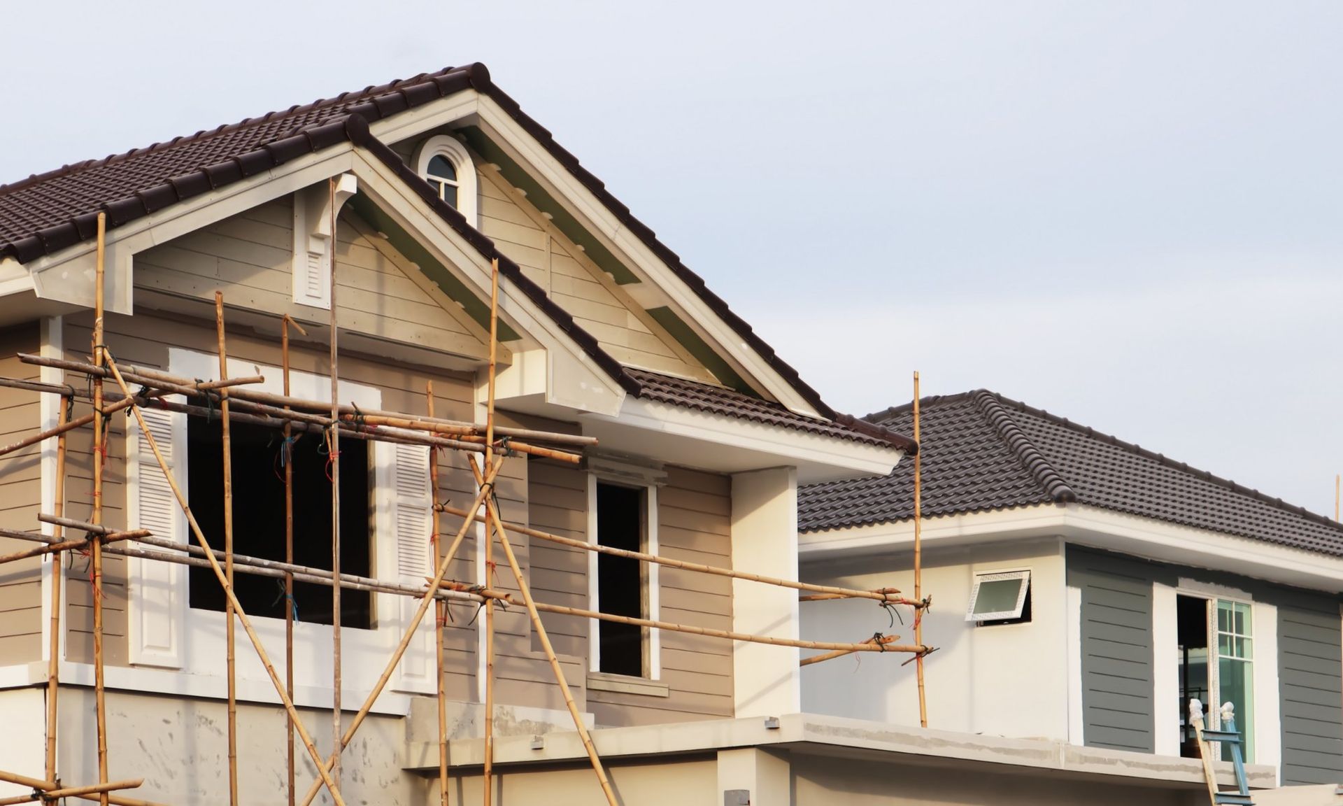 Two-story house under construction with brown roof, beige siding, scaffolding, and clear sky.