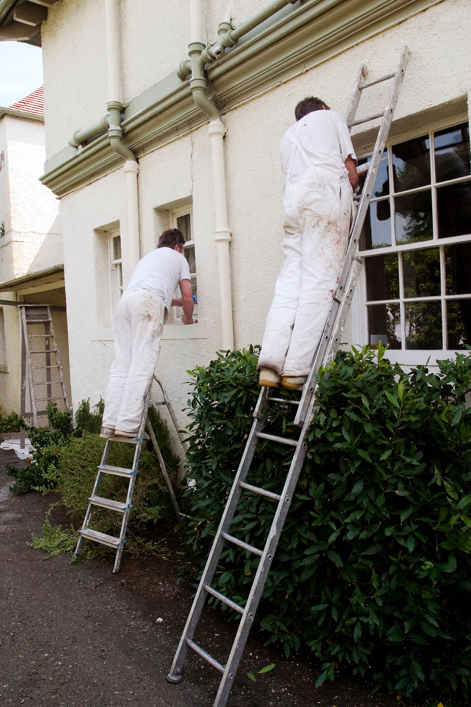 Person on an orange lift spraying paint on a house exterior. Windows are taped off.