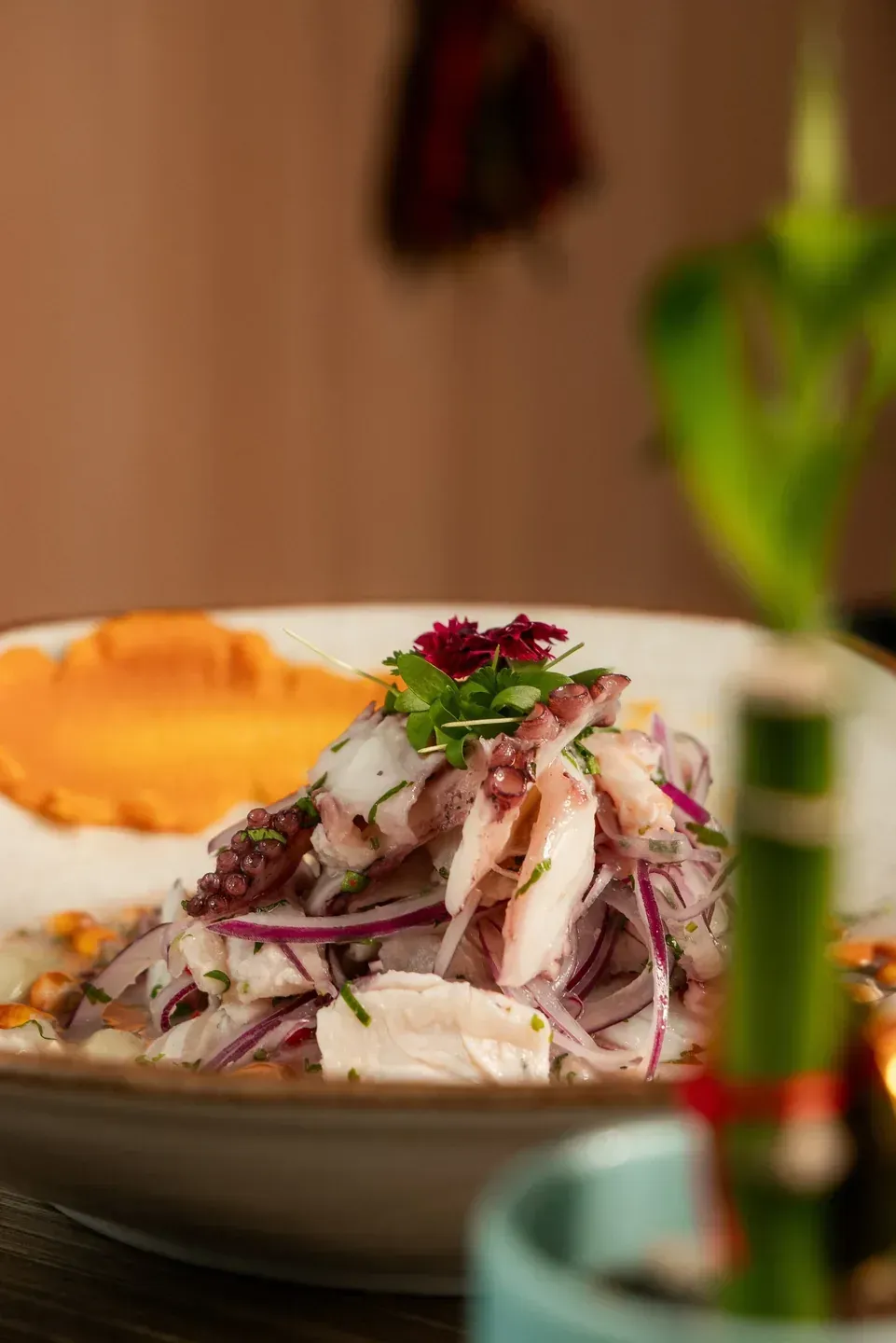 Close view of a ceviche-style fish dish with red onion and edible flowers at Enkai.