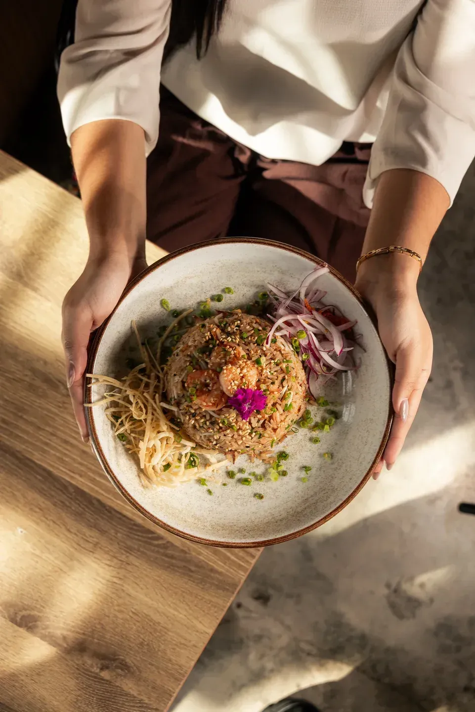 Server presenting Enkai fried rice topped with shrimp and edible flowers.