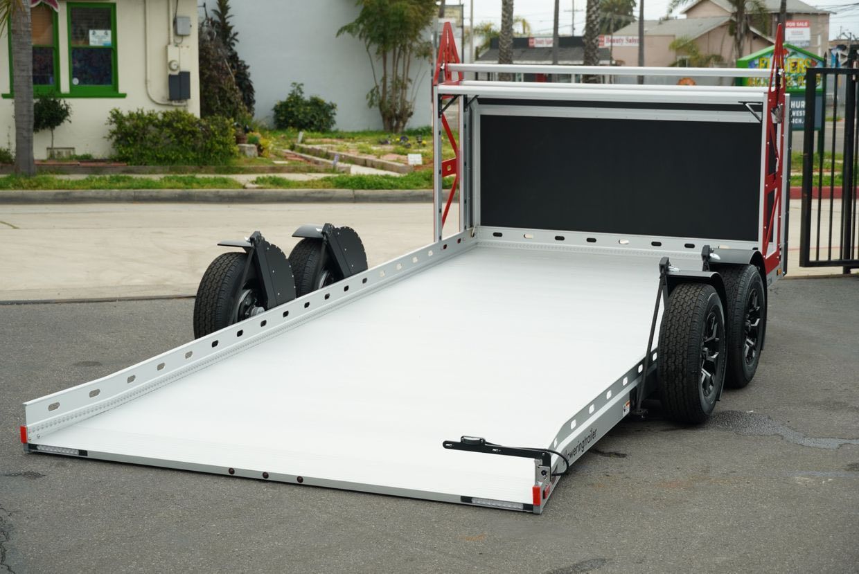 Empty, white-floored trailer with black backing, ready for loading. Wheels are visible. Outdoors, on asphalt.