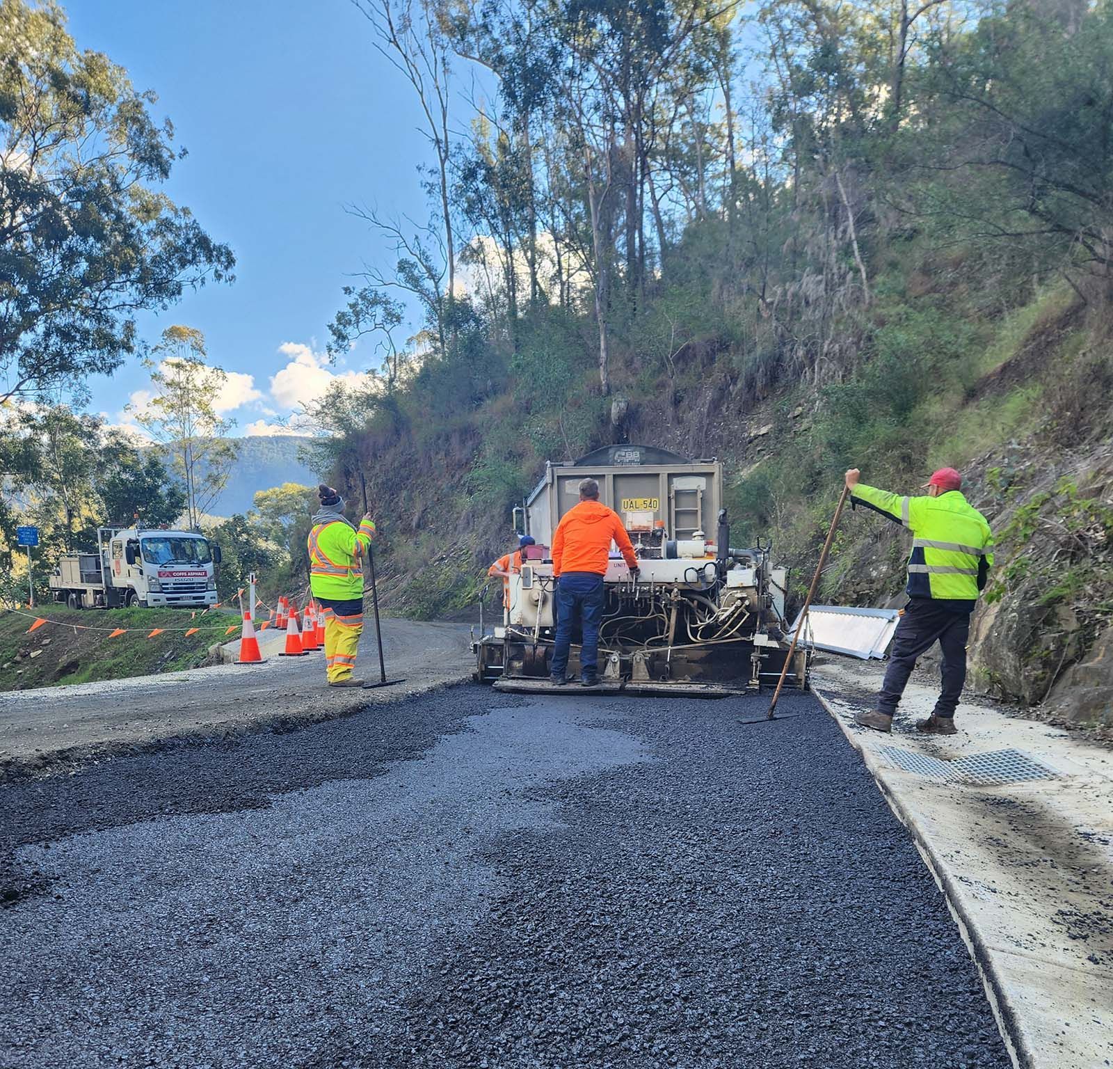 Road crew paving a rural road with an asphalt machine and workers in high-visibility gear