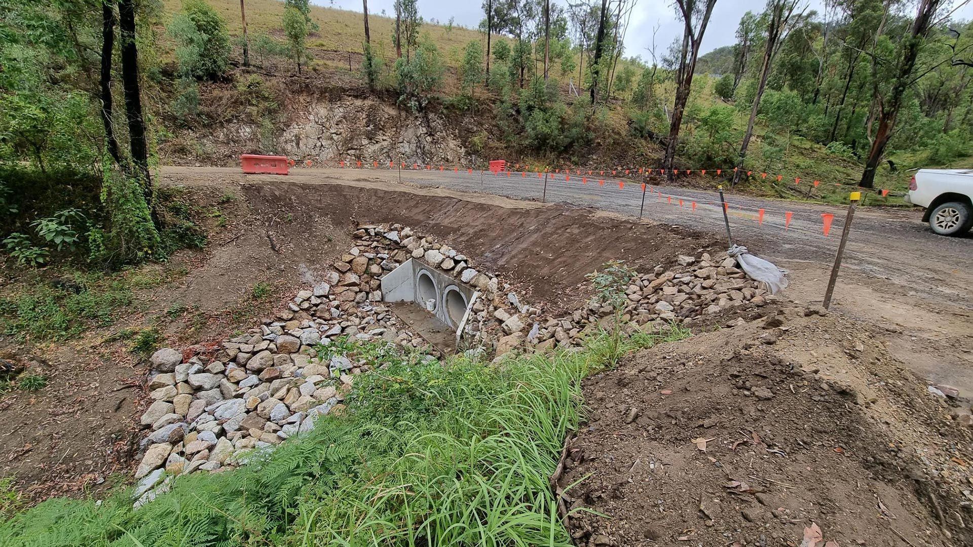Dirt road construction site with gravel piles, muddy track, and a white truck in the background
