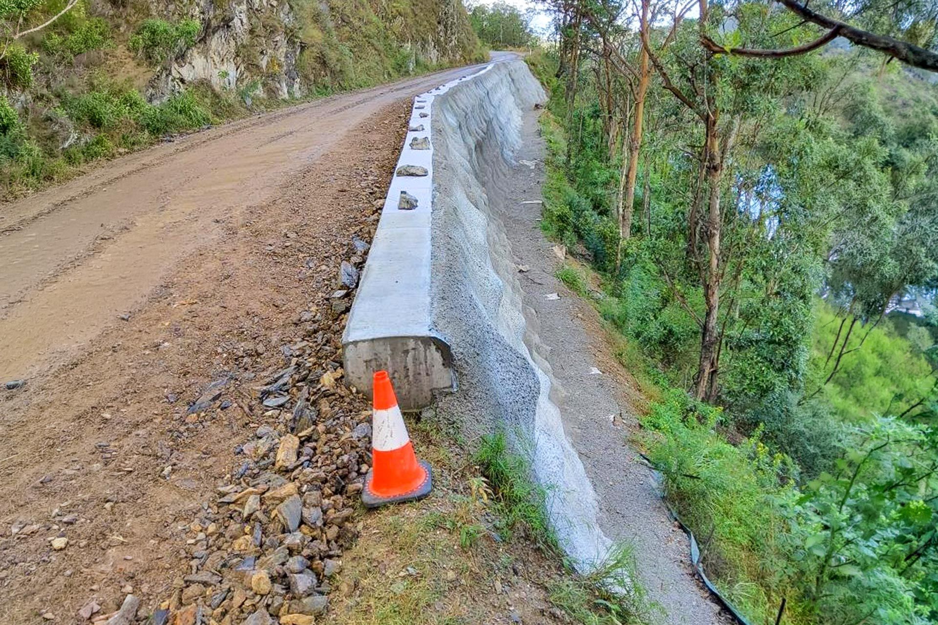 Damaged mountain road with a concrete barrier and orange traffic cone along a steep slope