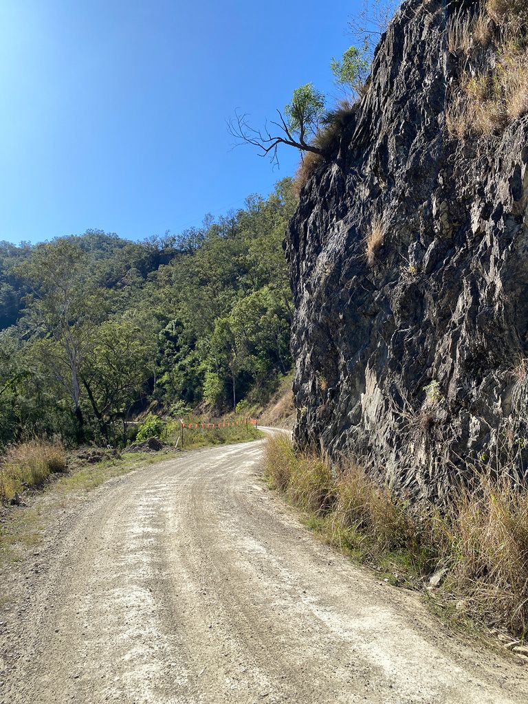 Dirt road curving beside a rocky cliff and green hillside under a clear blue sky