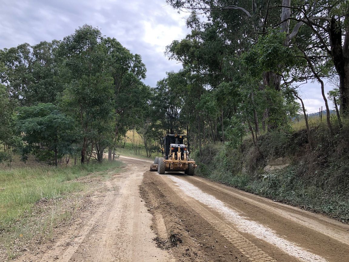 Road grader working on a dirt road in a wooded rural area