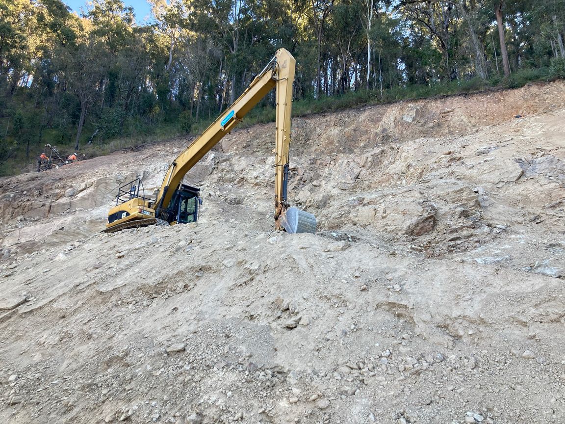 Yellow excavator digging into a rocky hillside at a construction site with trees in the background