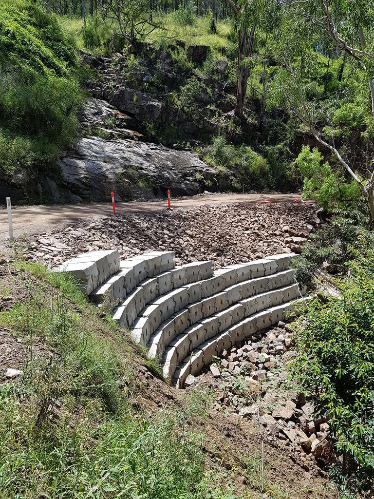 Terraced concrete retaining wall on a gravel slope beside a wooded hillside under construction