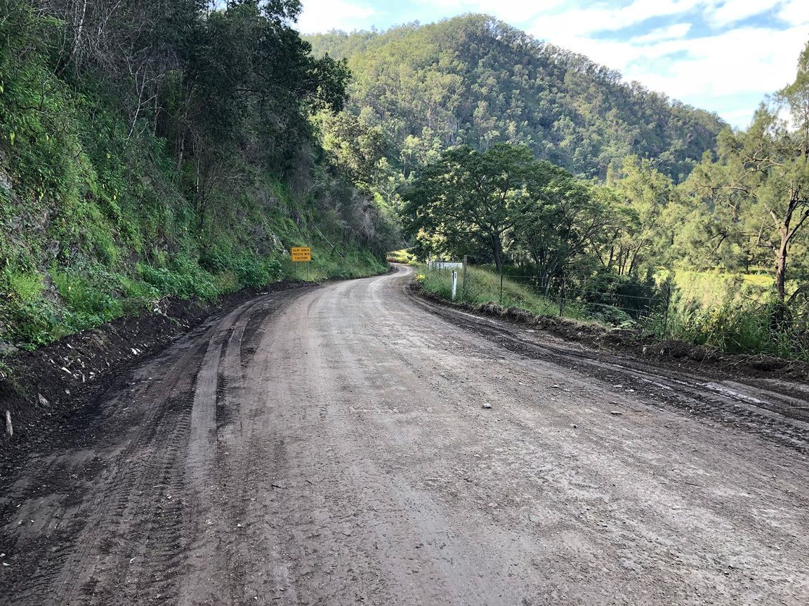 Curving dirt road through lush green hills under a partly cloudy sky