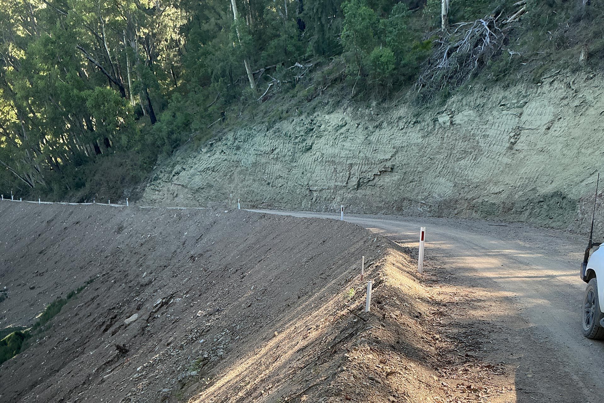 Mountain road cut into a steep hillside with dirt embankments and a car at the right edge