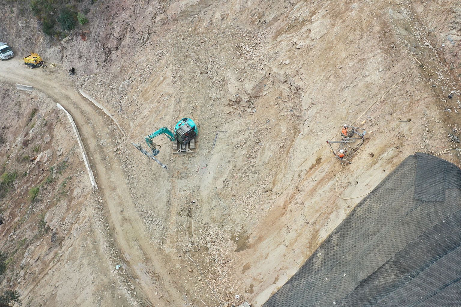 Aerial view of a turquoise excavator working on a dirt hillside construction site