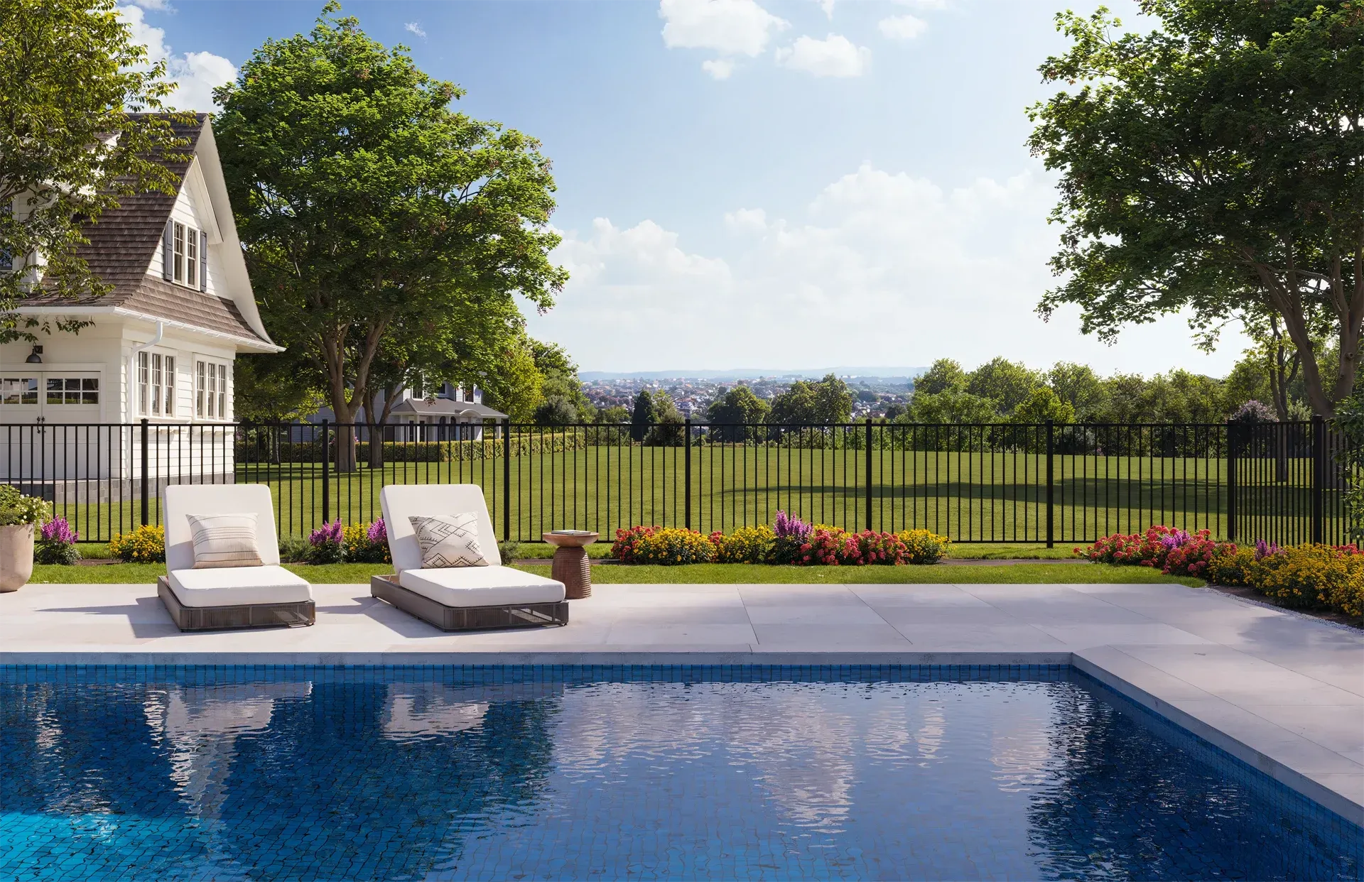 Poolside scene with lounge chairs, fenced yard, and white house on a sunny day.