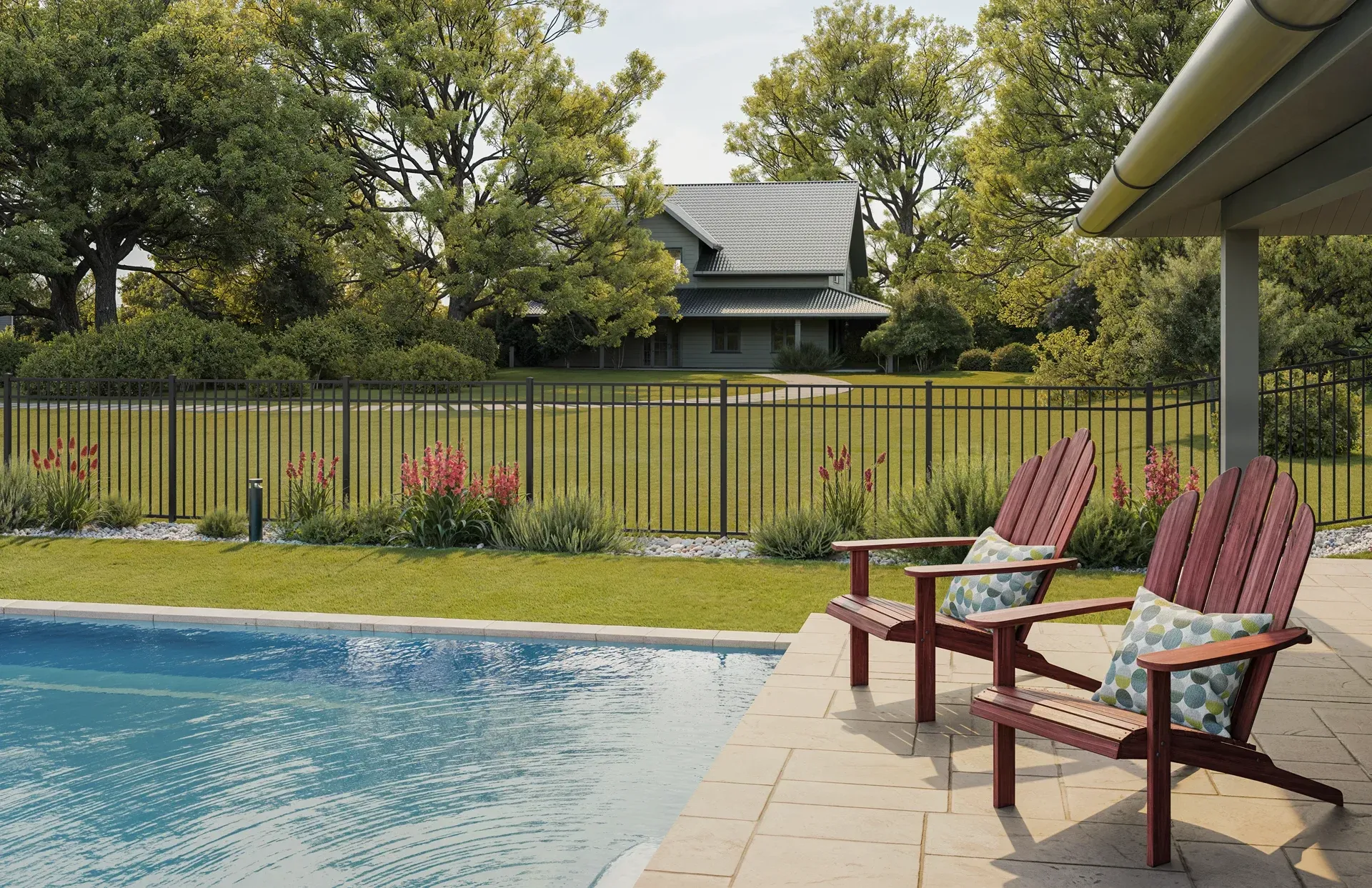 Two Adirondack chairs sit by a pool with a house in the background, behind a black fence.